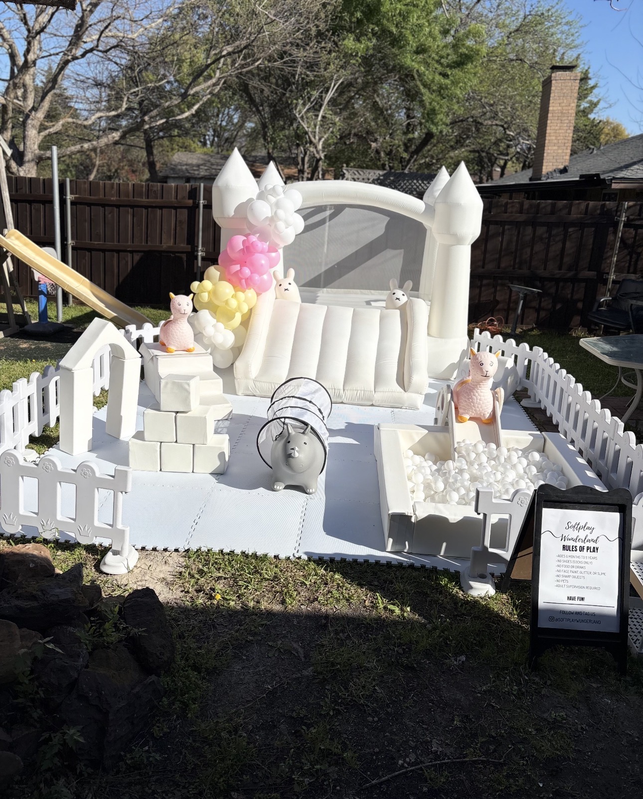 White bounce house with pink and yellow balloon garland and full soft play setup