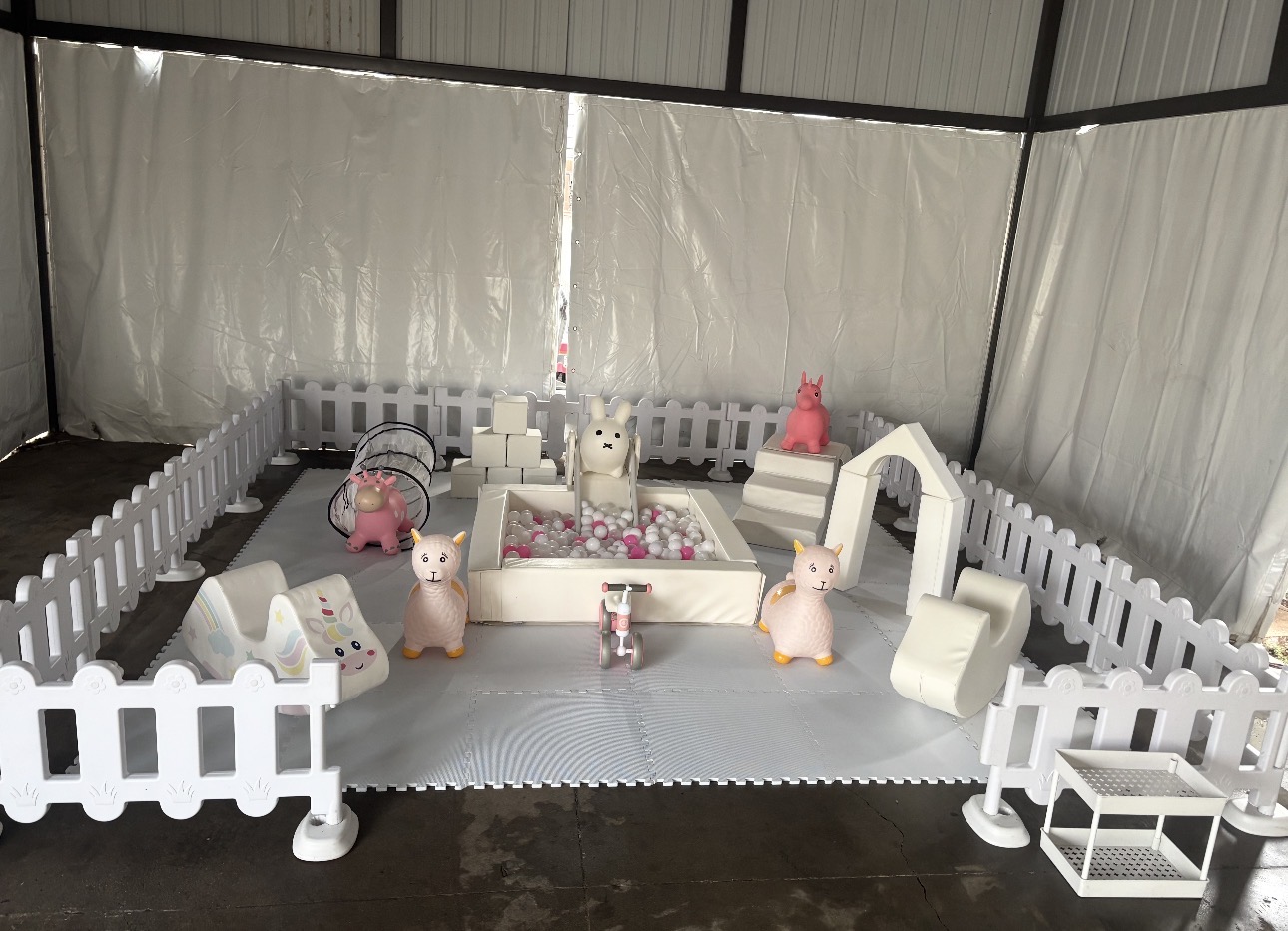 Indoor white soft play area with ball pit, fence and ride-on toys